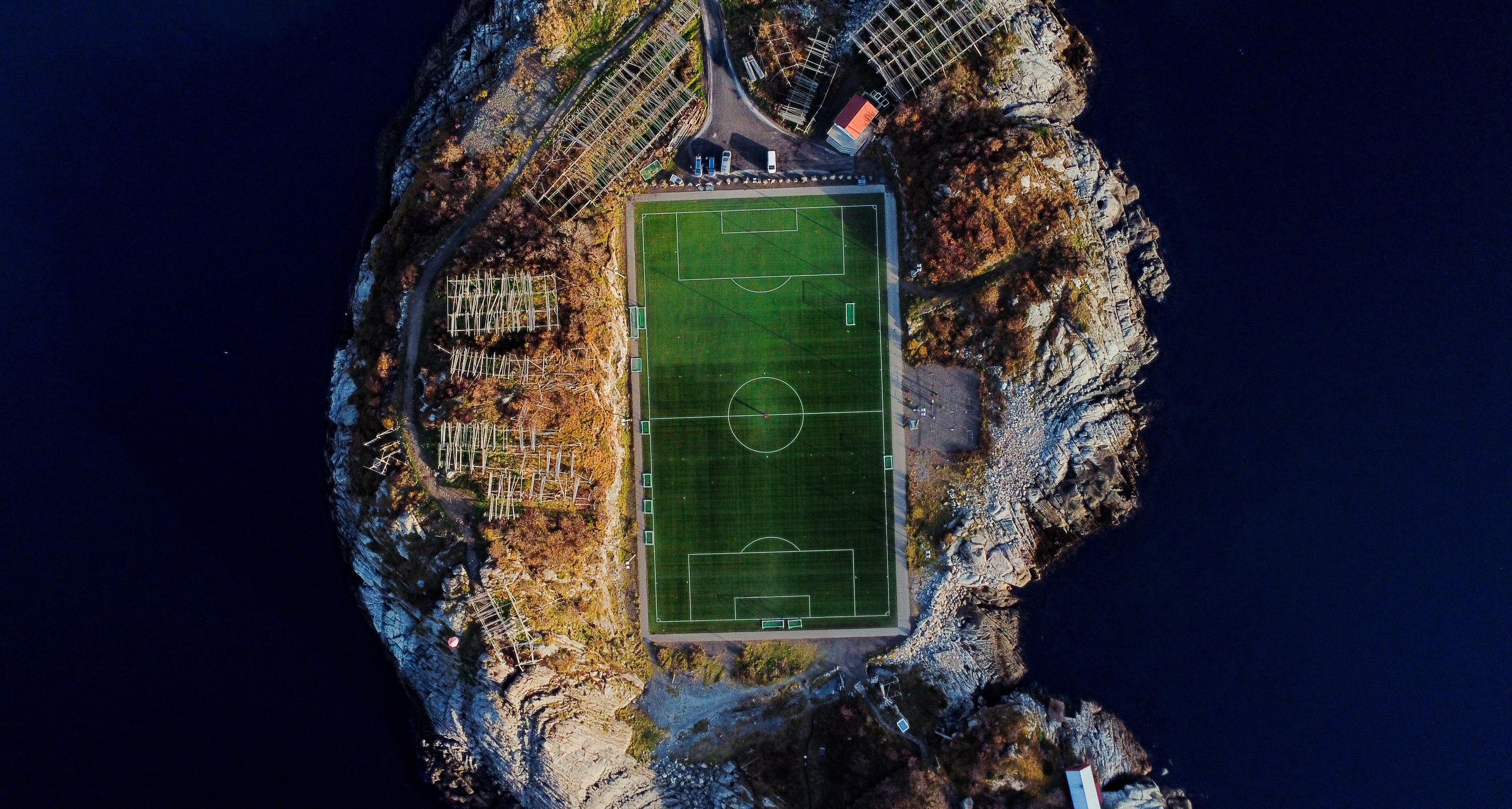 Photographié à la verticale, un terrain de football vert aux dimensions réglementaires occupe tout un îlot rocheux, cerné de broussailles automnales, de séchoirs en bois et d'une mer bleu nuit de tous côtés.